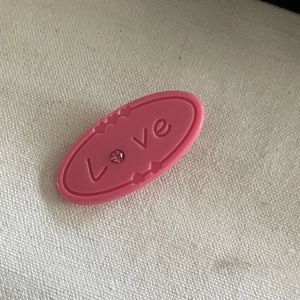 Détail d'une pince à cheveux ovale rose avec relief Love et strass étincelant
