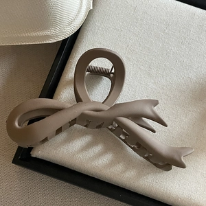 Pince à cheveux marron foncé mate en forme de nœud avec texture givrée sur fond de tissu beige