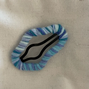 Cloud-shaped knitted wool hair clip with blue and purple yarn on a black metal BB base