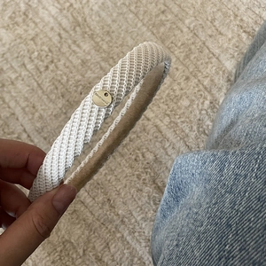 Detailed shot of a beige knitted headband with a gold 'HAND MADE' metal plate