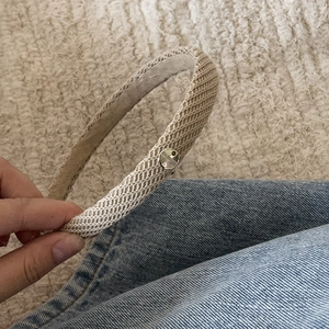 Macro shot of beige knitted headband featuring a silver metal plate with hand made text