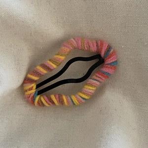 Detail of colorful woven yarn cloud-shaped snap hair clip on rustic linen background
