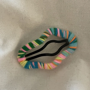 Close-up of cloud-shaped wool-wrapped hair clips with colorful yarn on fabric background