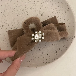 Détail d'une pince à cheveux en peluche marron avec nœud, cristaux et perles baroques
