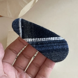 Detail of a navy blue plaid fabric hair clip with white stitching held in hand for size view