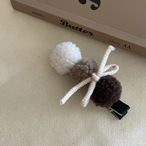 Détail d'une pince à cheveux avec pompons en polaire et nœud tissé sur tissu beige