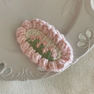 Pince à cheveux faite main au crochet avec fleurs roses et feuille verte sur plat blanc