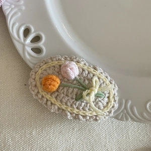 Détail de la pince à cheveux crochetée avec fleurs tricotées et nœud jaune sur céramique