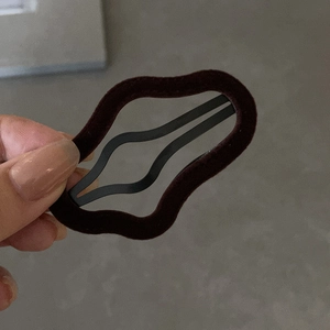 Close-up of a brown flocked wavy hair clip held in hand against a textured grey background