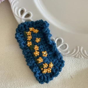 Détail d'une barrette fleurie crochetée à la main avec broderie orange sur laine bleue