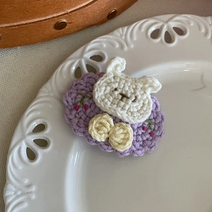 Détail d'une pince à cheveux ours tricotée main avec base de fleur mauve sur assiette