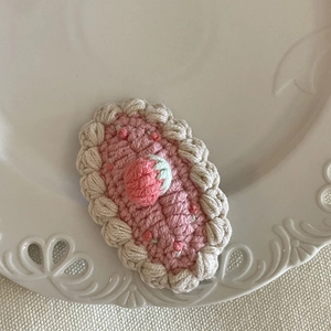 Détail d'une pince à cheveux en crochet avec fraise sur une assiette en céramique