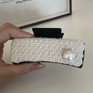 Close-up of white tweed fabric texture and large pearl detail on a hair claw clip