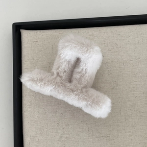 Close-up of a soft beige faux fur hair claw clip in an elegant textured tray