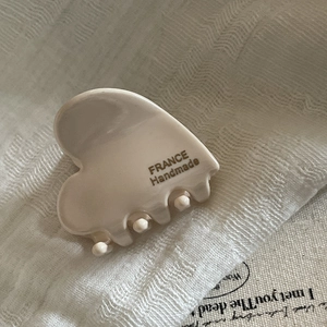Detail of a beige acetate heart hair claw with France Handmade text on linen background