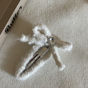 Détail de la barrette à cheveux en peluche blanche avec un strass brillant au centre