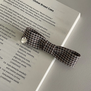 Detail of vintage houndstooth bow hair clip with silver brand logo on open book