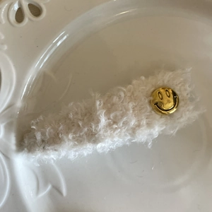 Détail d'une barrette en peluche blanc crème avec smiley doré sur plat en céramique