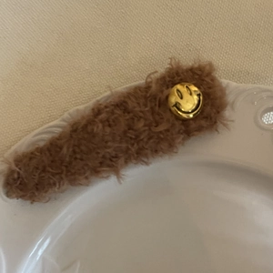 Gros plan d'une pince à cheveux en peluche marron avec un smiley doré sur une assiette