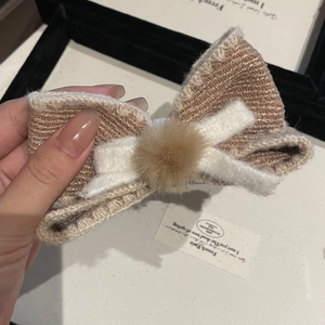 Detail of a brown knitted bow hair clip with a white felt layer and soft plush ball