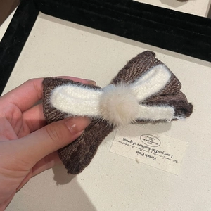 Detailed view of autumn brown knit bow hairclip with cream pompom and textured wool edges