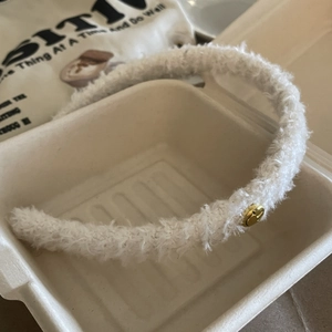 Détail du serre-tête en peluche blanche avec accent smiley doré dans un décor élégant