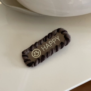 Barrette BB style Maillard avec texte HAPPY blanc et smiley posée sur un bureau blanc