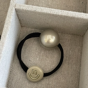 Elastic hair tie with champagne pearl and gold smiley face pendant on woven texture