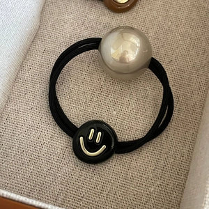 Elastic hair tie featuring champagne pearl and black smiley face charm in cream box