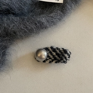 Houndstooth tweed hair clip with grey pearl detail on a beige textured background