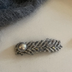Close-up of elegant tweed fabric hair clip with a grey pearl accent on a minimalist background