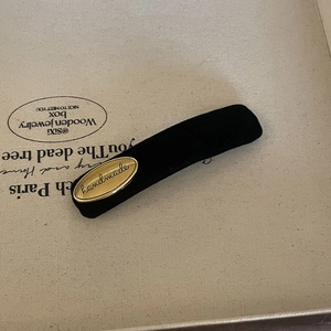 Close-up of black velvet hair clip with handmade gold metal tag and soft texture