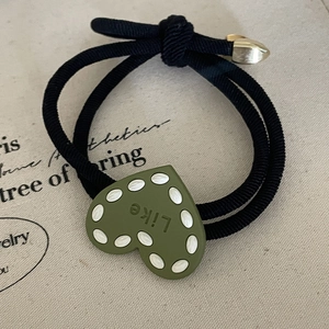 Green heart hair tie with white polka dots and golden metal hardware on black elastic rope