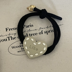Close-up of black elastic hair tie with green resin heart and Like inscription