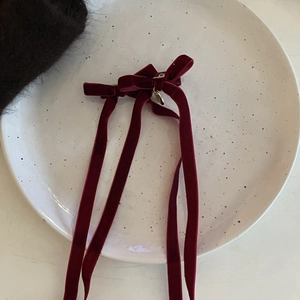 Elegant deep red velvet bow hair clip with long ribbons and a gold pendant on a ceramic plate