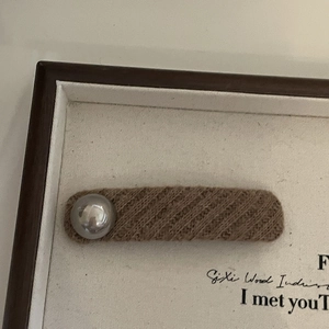 Brown knitted hair clip featuring a large silver metallic pearl on a white textured board