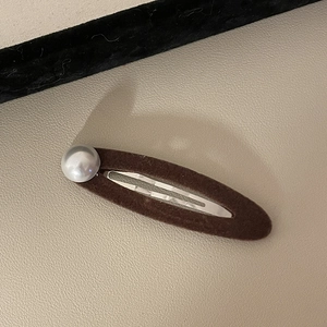 Detail von dunkelbrauner Samt-Haarklammer mit eleganter Perle auf Lederhintergrund
