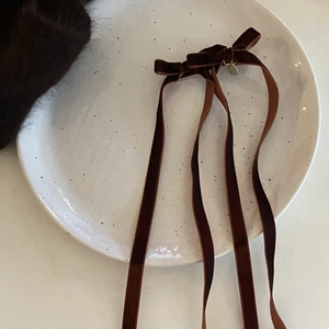 Close-up of deep brown velvet bow hair clip with long streamers and gold metal charm