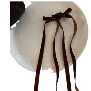 Brown velvet bow hair clip with long ribbons and a gold pendant on a ceramic plate