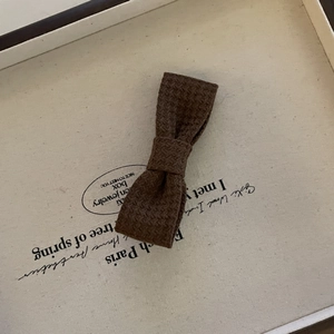 Macro detail of dark brown knitted bow hair clip with textured fabric on ivory tray