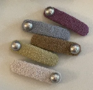 Gros plan de cinq barrettes en peluche colorée avec perles argentées aux tons Morandi