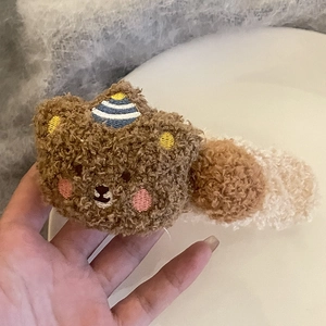 Détail de la pince à cheveux ours en peluche avec pompons colorés tenue à la main