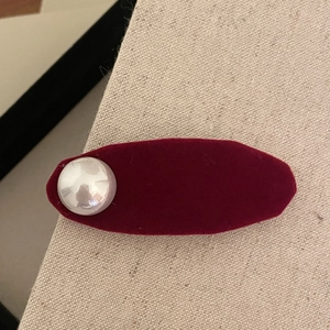 Elegant burgundy velvet oval hair clip with a pearl accent on beige fabric background