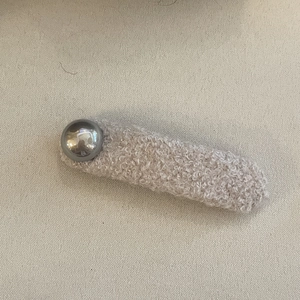 Détail d'une grande pince à cheveux en peluche avoine avec un bouton métallique brillant
