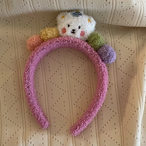 Bandeau en peluche rose avec un ours blanc et des pompons colorés sur fond beige