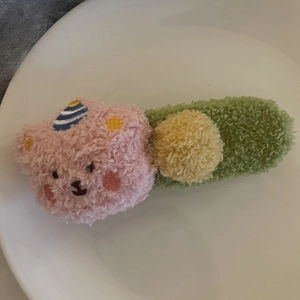 Vue détaillée de la barrette ours en peluche rose avec pompon jaune et base verte