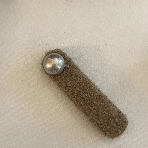 Gros plan sur la barrette en peluche marron ornée d'une grande perle blanche