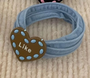 Close-up of light blue elastic hair tie with brown heart-shaped pendant and Like text