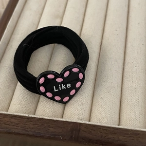 Elastic black hair tie with a black heart charm featuring Like text and pink dots