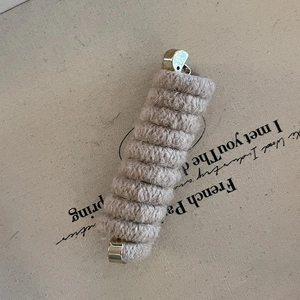 Detailed macro view of the soft oatmeal wool texture and gold metal caps on the hair tie
